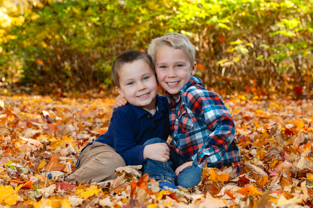 Two brothers playing in autumn leaves during a family portrait session at the Dominion Arboretum in Ottawa