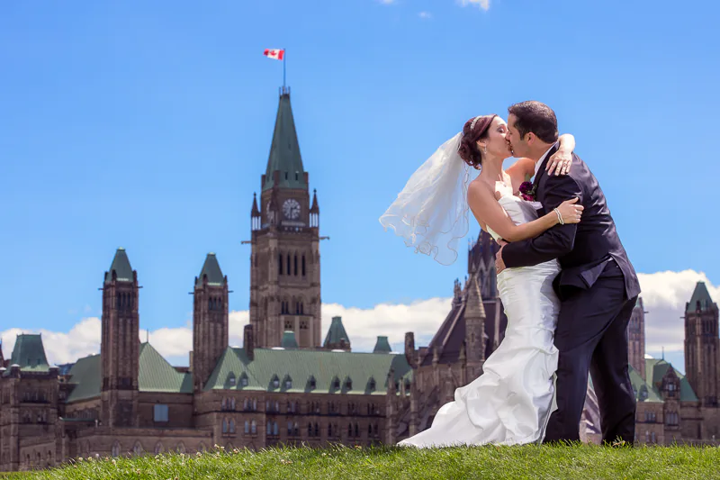 A couple kiss in front of Canada's Parliament Hill during their wedding day.   A wedding photo by Jeffrey Meyer.