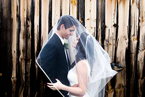 A bride and groom pose next to rustic barn wood during their countryside wedding