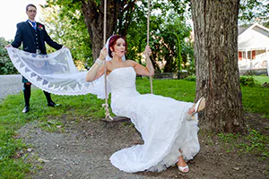 A bride plays on a swing while her groom holds her long veil