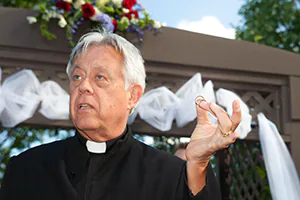 A pastor blesses two rings held together by his index finger and thumb