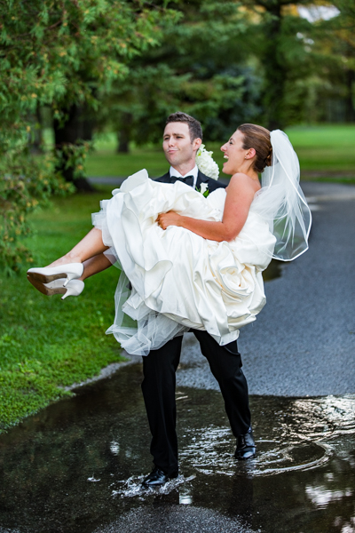 A groom lifts his bride over a puddle